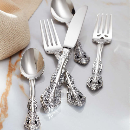 Ornate silver flatware set including spoon, knife, and forks on a marble surface.