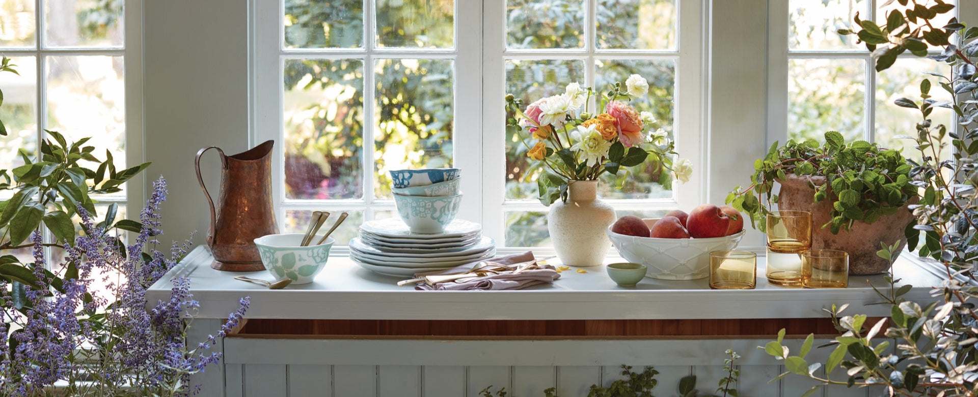 Rustic kitchen counter with dishes, flowers, and fruit.