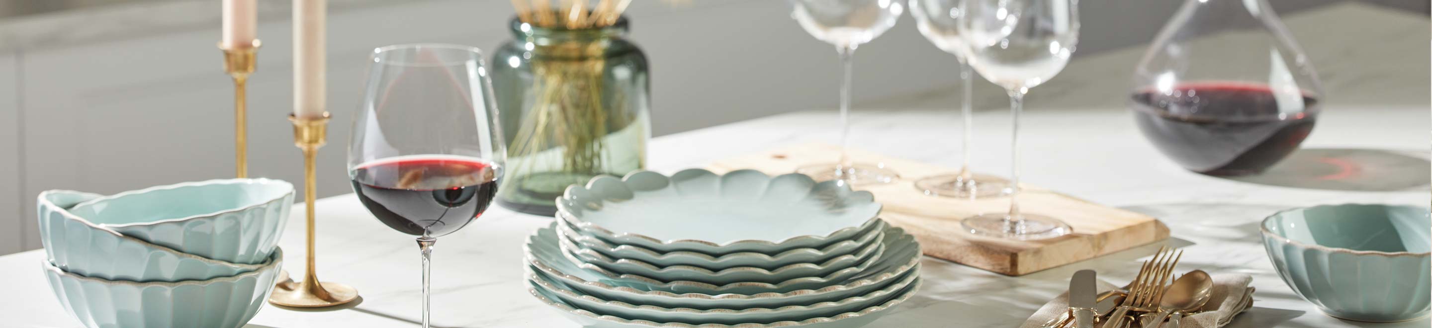 stacked blue dinnerware on a table with wine glasses, candles, a vase, and decanter.