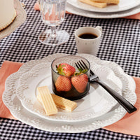 Table with a black and white tablecloth and Chelse Muse dinnerware with a glass of strawberries and a black fork.