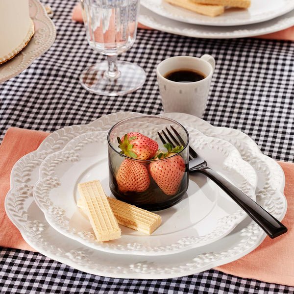 Table with a black and white tablecloth and Chelse Muse dinnerware with a glass of strawberries and a black fork.