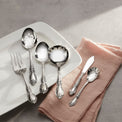 Silver cutlery set on a white plate with a pink napkin on a gray surface