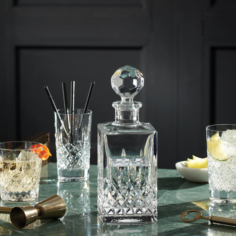 Crystal decanter with cocktail glasses and bar tools on a dark surface