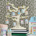 Decorative tree with small house ornaments against a leaf-patterned wall.