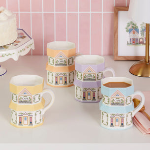 Set of colorful mugs with house designs on a table against a pink tiled wall.