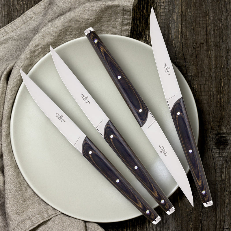 Set of four steak knives with wooden handles on a light green plate.